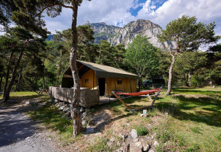 Tienda safari Villatent Wood en Camping River, Francia, rodeada de pinos y montañas pintorescas.