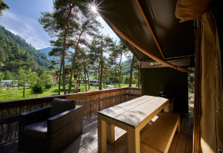 Vista desde la terraza de una tienda safari en Camping River, Francia, rodeada de árboles y montañas verdes.