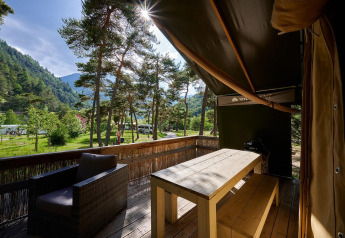 Vista desde la terraza de una tienda safari en Camping River, Francia, rodeada de árboles y montañas verdes.