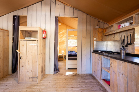 Vista interior de la tienda safari Villatent Wood con mobiliario de madera en Camping River, Francia.