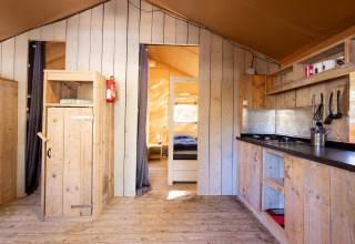 Binnenaanzicht van de Villatent Wood safaritent met houten meubilair en keuken bij Camping River in Frankrijk.