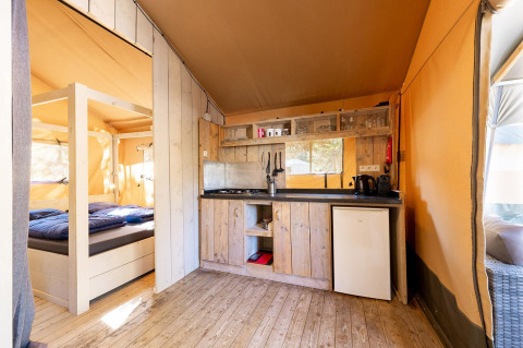Binnenzicht van Villatent Wood safaritent op Camping River in Frankrijk met keuken en bed.