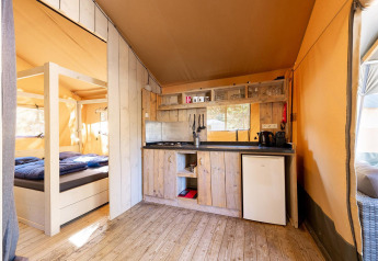 Vista interna della tenda safari Villatent Wood al Camping River in Francia, con cucina e letto.