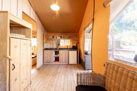 Interior de una tienda safari con muebles de madera en Villatent Wood, Camping River, Francia, con cocina y sala.