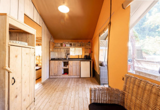 Innenraum eines Safari-Zeltes Villatent Wood auf Camping River, Frankreich, mit Holzmöbeln und Küchenbereich.