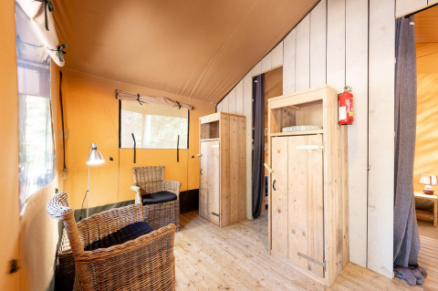 Binnenkant van de Villatent Wood safaritent op Camping River in Frankrijk met rotan stoelen en houten vloer.