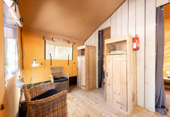 Interior de la tienda safari Villatent Wood en Camping River, Francia, con sillas de mimbre y suelo de madera.