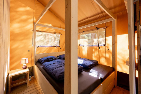 Binnenzicht van de Villatent Wood safaritent op Camping River in Frankrijk met bed en nachtkastje.