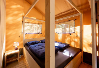 Binnenzicht van de Villatent Wood safaritent op Camping River in Frankrijk met bed en nachtkastje.