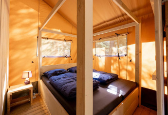 Interior de la tienda safari Villatent Wood en Camping River, Francia, con cama y mesa de noche visible.