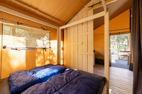 Foto interior de una tienda safari Villatent Wood con cama doble en Camping River, Francia.