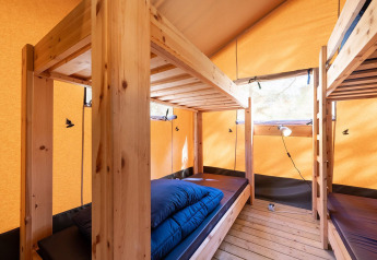 Interior de una tienda safari Villatent Wood en Camping River, Francia, con literas de madera y ropa de cama.