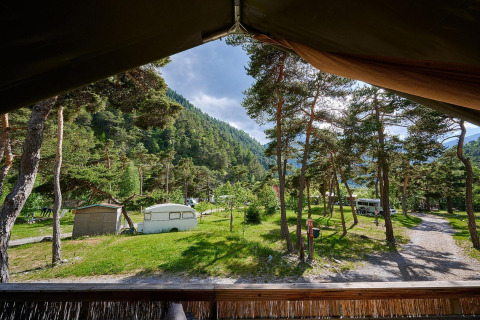 Vista desde una tienda safari en Villatent Wood en Camping River, Francia, rodeada de árboles y montañas verdes.