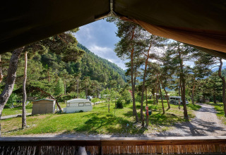 Blick aus einem Safarizelt bei Villatent Wood auf Camping River in Frankreich, umgeben von Bäumen und Bergen.