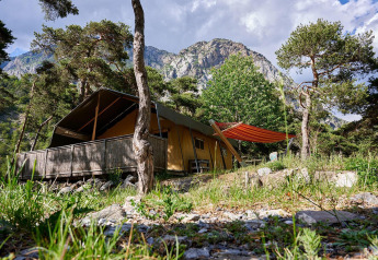 Tenda safari Villatent Wood al Camping River in Francia, circondata da alberi, montagne e cielo azzurro.