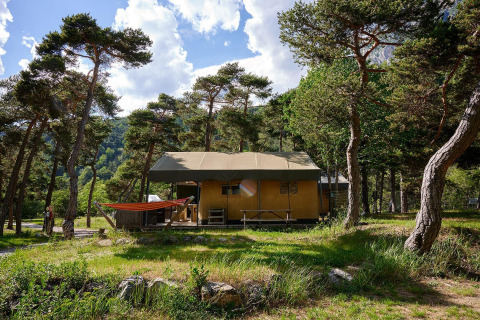 Safari teltet Villatent Wood på Camping River i Frankrig, omgivet af træer og natur under en blå himmel.