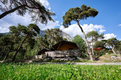 Safaritent Villatent Wood bij Camping River in Frankrijk, omgeven door bomen en bergen op een zonnige dag.