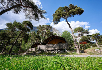 Safarizelt Villatent Wood auf Camping River in Frankreich, umgeben von Bäumen und Bergen bei Sonnenschein.