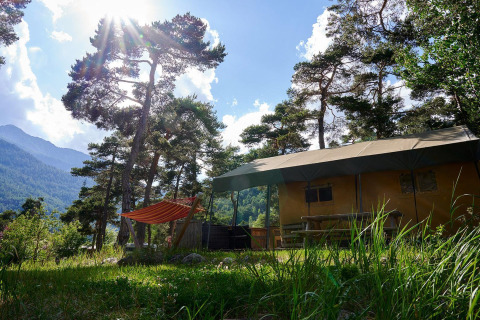 Tienda safari Villatent Wood en Camping River, Francia, rodeada de árboles y paisajes montañosos soleados.