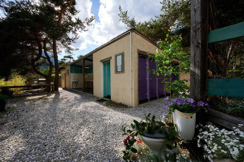 Sanitairgebouw bij Villatent Wood op Camping River in Frankrijk met bloemen en grindpad.
