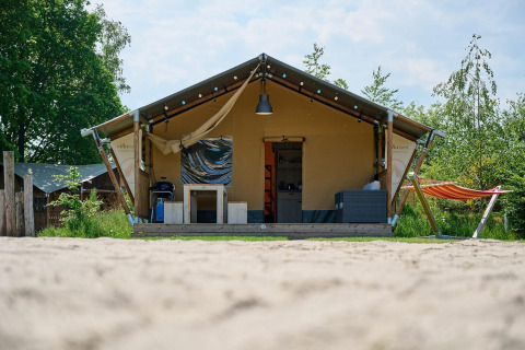 Tienda safari Villatent Nomad en Vakantiepark Sallandshoeve, Países Bajos, con hamaca y terraza acogedora.