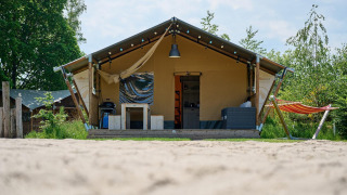 Tienda safari Villatent Nomad en Vakantiepark Sallandshoeve, Países Bajos, con hamaca y terraza acogedora.