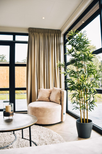 Rincón de salón moderno con sillón redondo, ventanales grandes, cortinas claras y planta en Villa Nautica Deluxe.