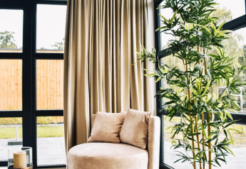 Rincón de salón moderno con sillón redondo, ventanales grandes, cortinas claras y planta en Villa Nautica Deluxe.