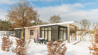 Luxe lodge met sauna in de sneeuw op Vakantiepark Hölte, Nederland, omgeven door bomen en een winterlandschap.