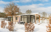 Luxe lodge met sauna in de sneeuw op Vakantiepark Hölte, Nederland, omgeven door bomen en een winterlandschap.