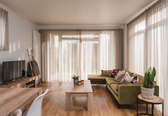 Soggiorno luminoso e moderno in un lodge di lusso al Vakantiepark Hölte, Paesi Bassi, con divano verde e grandi finestre.