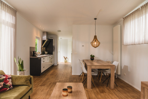 Binnenzicht van een luxelodge met eettafel, keuken, zetel en grote ramen in Vakantiepark Hölte.