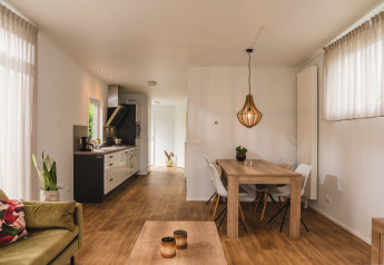 Binnenzicht van een luxelodge met eettafel, keuken, zetel en grote ramen in Vakantiepark Hölte.