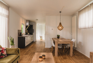 Interieur van een luxelodge met eettafel, keuken, bank en grote ramen in Vakantiepark Hölte.