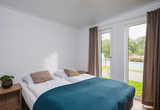 Camera moderna con letto matrimoniale, grandi finestre e vista sul giardino a Vakantiepark Hölte, Paesi Bassi.