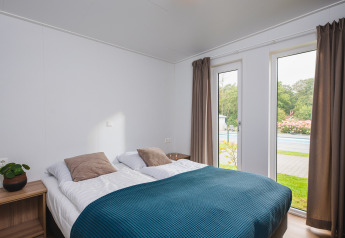 Camera moderna con letto matrimoniale, grandi finestre e vista sul giardino a Vakantiepark Hölte, Paesi Bassi.