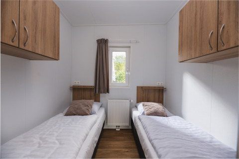 Modernes Lodge-Zimmer mit zwei Einzelbetten, Holzschränken und Fenster im Vakantiepark Hölte, Niederlande.