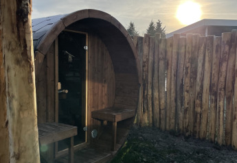 Ronde houten sauna bij zonsondergang in de tuin van een luxueuze lodge in Vakantiepark Hölte, Nederland.