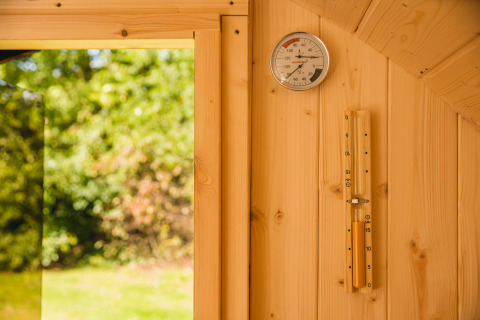 Innenansicht einer Luxushütte mit Sauna, Holzwand, Thermometer und Blick auf den grünen Garten in den Niederlanden.