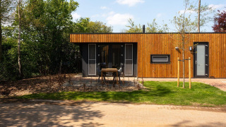 Moderne Holzhütte Oak Lodge im Vakantiepark Hölte, Niederlande, mit Terrasse und umgeben von Bäumen.