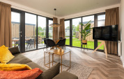 Moderne opholdsstue i Oak Lodge ved Vakantiepark Hölte, Holland, med store vinduer og minimalistisk indretning.