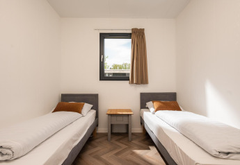 Two single beds with white linens and orange cushions in Oak Lodge, Vakantiepark Hölte, Netherlands.