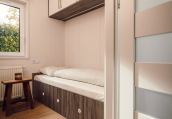 Petit espace nuit dans une tiny house avec un lit simple, des placards en hauteur et une déco minimaliste.