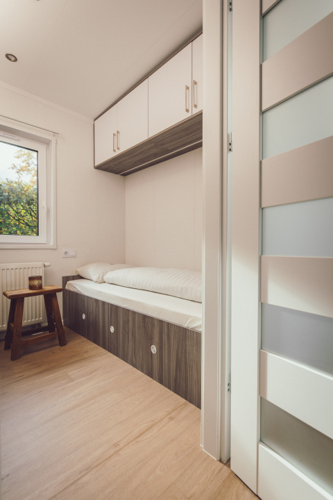 Pequeña zona de descanso en una tiny house con cama individual, armarios superiores y decoración minimalista.