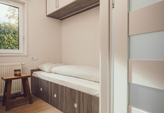 Et lille soveområde i et tiny house med enkeltseng, indbyggede skabe og minimalistisk indretning.