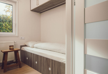 Petit espace nuit dans une tiny house avec un lit simple, des placards en hauteur et une déco minimaliste.