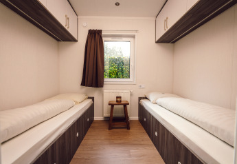 Deux lits simples dans une chambre minuscule d'une tiny house, avec fenêtre et sol en bois clair.