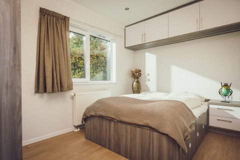 Dormitorio luminoso en una tiny house con cama doble, almacenaje empotrado y ventana grande con vista verde.