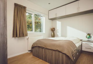 Dormitorio luminoso en una tiny house con cama doble, almacenaje empotrado y ventana grande con vista verde.