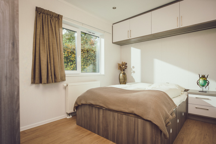 Helles Schlafzimmer in einem Tiny House mit Doppelbett, Einbauschränken und großem Fenster mit Gartenblick.